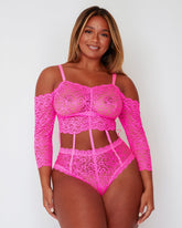 Model wearing the Alix Bodysuit in vibrant Pink, featuring floral lace throughout, an off-the-shoulder neckline, long lace sleeves, and statement cut-out detailing through the waist connected by delicate strap accents.