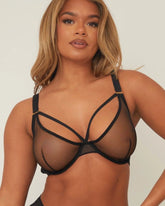 Woman wearing a black strappy bra against a plain background