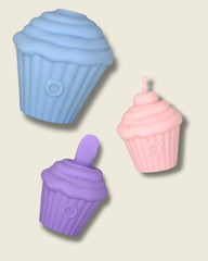Three silicone cupcake-shaped discrete sex toys in blue, purple, and pink on a beige background.