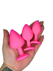 Three pink silicone butt plugs held in a hand against a white background