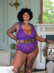 Plus size model posing indoors in the Hallie bralette and brief set in Passion Purple from Tutti Rouge, featuring sheer lace cups and high-waisted lace briefs.