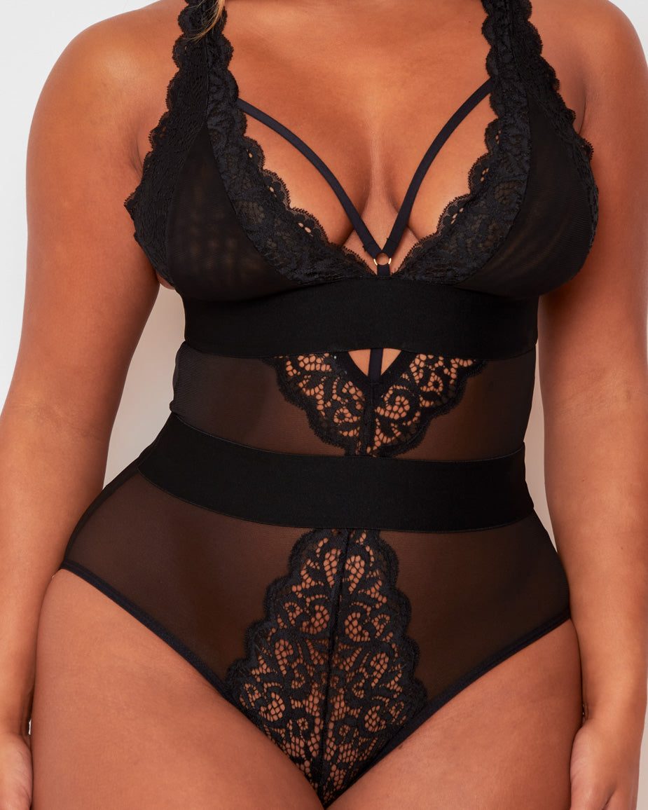 Model posing in the Alicia Bodysuit in Black by Tutti Rouge, displaying sheer mesh panels, intricate lace detailing, and a supportive, figure-enhancing fit.
