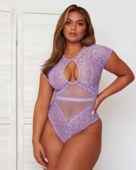 Model wearing the Ember Bodysuit in Lavender, featuring delicate floral lace, sheer polka-dot mesh panels, a keyhole neckline, short lace sleeves, and a flattering high-leg silhouette.